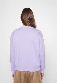 Lila sweatshirt i bomullsblandning med rund hals och ribbade ärmslut, kombinerad med en veckad beige kjol.