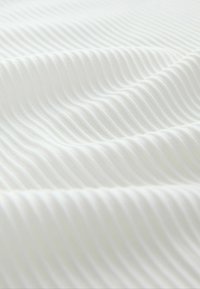 Fehér szövet közeli kép, amely diagonális bordázott textúrával és lágy redőkkel rendelkezik, hullámszerű mintát alkotva.