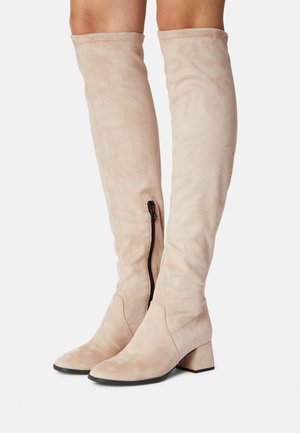 Beiget polven yli ulottuvat pehmeästä mokkanahasta valmistetut saappaat, joissa on sivuvetoketju, teräväkärkiset varpaat ja lohkokorko.