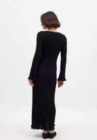 Melna ribota adīta kleita ar garām, izplestām piedurknēm un izgrieztu muguru. Apakšmalai ir viļņota forma, kas piedāvā teksturētu izskatu.