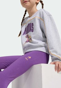 Szara bluza z napisami i grafiką w kolorze fioletowym, zestawiona z fioletowymi legginsami z logo. Gładka faktura, luźny krój.