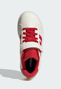 Bílé tenisky s červenými tkaničkami, červeným jazykem a červenými proužky Adidas, s páskem na suchý zip přes vršek.