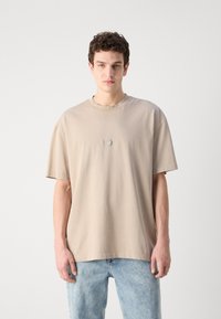 Beige oversize T-särk lühikeste varrukatega, ümar kaelus ja ringikujuline detail rinnal. Valmistatud pehmest puuvillamisest.