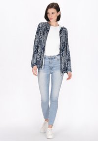 Felpa con zip di colore navy con motivo paisley, abbinata a una t-shirt bianca e jeans skinny blu chiaro, indossata con sneakers bianche.