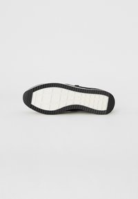 Semelle de sneaker noire avec une semelle extérieure en caoutchouc texturé et une semelle intermédiaire blanche. Présente un motif de carrés en grille pour une meilleure traction et adhérence.