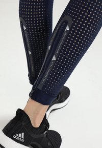 Merinavyyn kunto leggingsit, joissa on rei'itetty kangas, sivuvetoketjut ja mustat yksityiskohdat. Yhdistetty mustiin urheilukenkään.