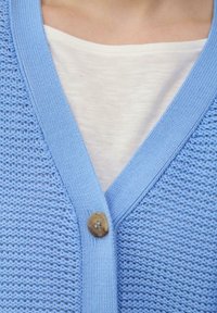Hellblauer gestrickter Cardigan mit V-Ausschnitt und strukturiertem Muster, ausgestattet mit einem braunen Knopf und einer weißen Innenschicht.