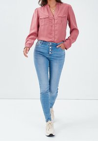 Helles rosa Knopfhemd mit zwei Brusttaschen, kombiniert mit hellblauen hochgeschnittenen Skinny-Jeans mit Fünf-Knopf-Verschluss und dezentem Stretch.