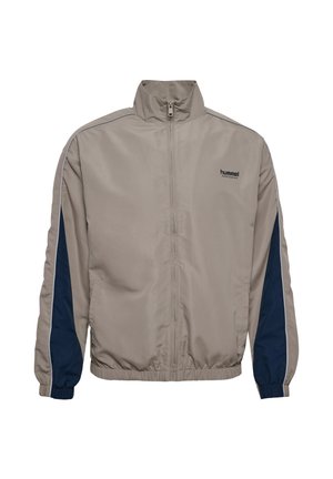 Beżowa kurtka zapinana na zamek z wysokim kołnierzem, granatowymi panelami po bokach, elastycznymi mankietami i dołem, z małym logo na piersi. Gładka faktura tkaniny.