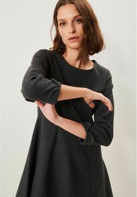 Tummanharmaa mekko pitkillä hihoilla, pyöreällä kaula-aukolla ja väljällä A-linjalla. Pehmeä tekstuuri, jossa on hienovaraisia saunatikkauksia.