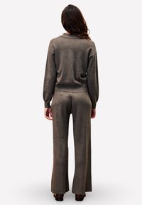 Pull en maille brun avec une coupe décontractée et un ourlet côtelé, associé à un pantalon large assorti, les deux dans une texture douce et une teinte neutre.