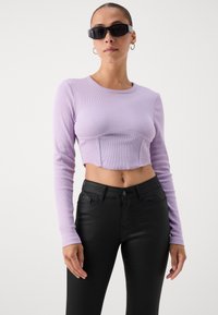 Licht paarse geribde langemouwen crop top met een ronde halslijn, gecombineerd met zwarte strakke broek. Accessoires zijn onder andere zwarte zonnebrillen.