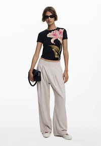 Svart t-shirt med rosa blomdesign, ljusbeige vida byxor, svart handväska och solglasögon. Mjukt tyg, ledig passform.