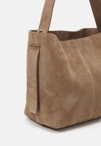 Brown suede tote bag with a smooth texture, featuring a wide opening and a side tab accent. Sturdy straps for carrying.