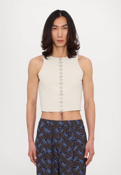 Crop top beige à côtes avec un col haut et un détail de bouton central, associé à un pantalon à motifs marron avec des accents bleus.