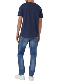 Granatowy bawełniany t-shirt z krótkim rękawem i okrągłym dekoltem, zestawiony z jasnoniebieskimi dżinsami denim z klasycznymi kieszeniami oraz białymi trampkami.