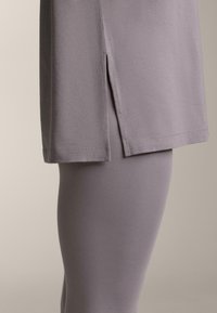 Voľný levanduľový top s bočným rozparkom, v páre s priliehavými legínami v rovnakom odtieni, obe z mäkkej, hladkej tkaniny.