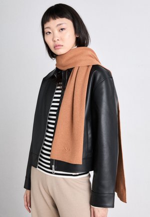 Une écharpe en maille marron repose sur une veste en cuir noire, portée avec un haut rayé noir et blanc. Le tissu semble doux, avec un design épuré.