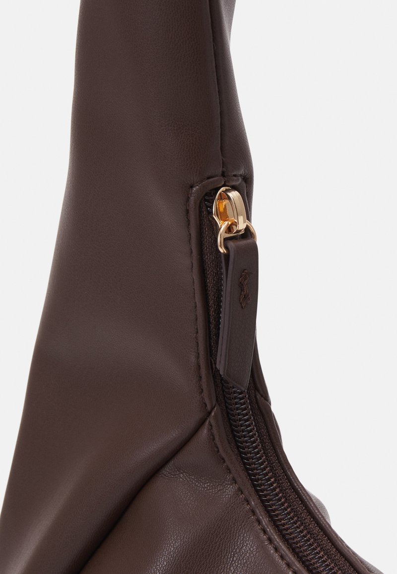 Borsa in pelle marrone con texture liscia e forma curva. Presenta una zip in tonalità oro e un piccolo tirazip in pelle con dettaglio del marchio.