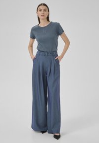 Blau gestreiftes T-Shirt mit Rundhalsausschnitt, kombiniert mit hoch sitzender, weiter gestreifter Hose in Dunkelblau, ausgestattet mit einem Gürtel und Falten.