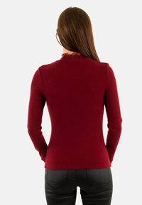 Maglia a maniche lunghe a coste in bordeaux con scollatura arricciata. Il tessuto sembra morbido e aderente, adatto per essere indossato a strati o da solo.