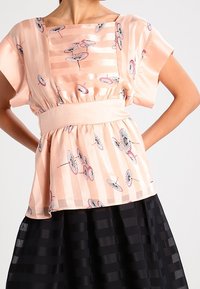 Top de satén durazno con rayas verticales y patrones de paraguas; cintura ceñida; mangas cortas; combinado con una falda negra texturizada.