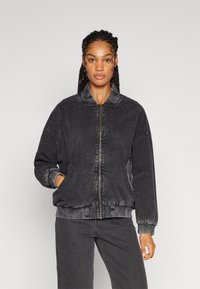 Black denim jacket with a zip front, ribbed cuffs, and side pockets. Features a relaxed fit and a textured finish.