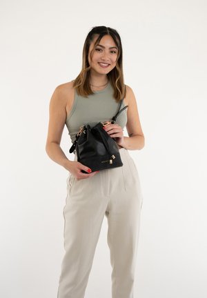 Black leather bucket bag with a drawstring closure, gold hardware accents, and a detachable strap, held by a person wearing a light tank top.