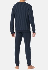 Tmavě modrý loungewear set s vertikálními pruhy, obsahující top s dlouhým rukávem a kalhoty s elastickým pasem. Hladká, měkká látka, bez viditelných vzorů.