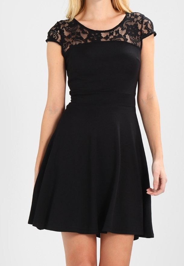 Femme portant une robe noire avec un col en dentelle florale et des manches courtes, taille cintrée et jupe évasée sur fond uni.