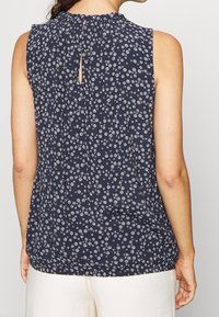 Mörkblå ärmlös topp med blommönster, med en dra-n uppläggning vid halsen, nyckelhålsdetalj bak, och en avslappnad passform vid midjan.