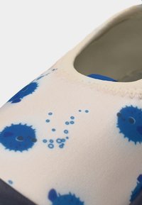 Κοντινό πλάνο ενός λευκού παπουτσιού με σχέδια μπλε φουσκωτού ψαριού και φυσαλίδων, δείχνοντας ραμμένη άκρη και απαλή υφή.