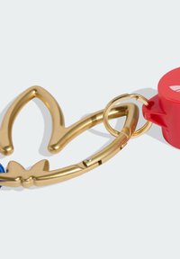 Złoty brelok w kształcie korony, wyposażony w niebieski materiałowy pasek oraz czerwony plastikowy element z logo.