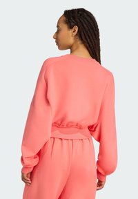 Koralový svetor so strihom na telo, s okrúhlym výstrihom, rebrovaným pásom a so spustenými ramennými švami. Hladká textúra; skombinovaný s rovnakými nohavicami.