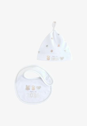 Cappellino bianco in cotone per bebé con nodo superiore e stampe di animali sparse; bavaglino coordinato con ricamo "Nato nel 2026" e motivi di animali.