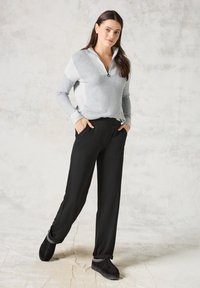 Grau-weißer Farbblock-Pullover mit Reißverschluss und geripptem Kragen, kombiniert mit schwarzen maßgeschneiderten Hosen und schwarzen Slippern mit Akzenten.