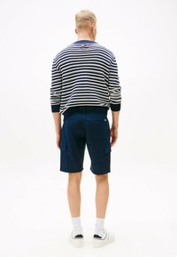 Granatowe szorty cargo z dwoma bocznymi kieszeniami i płaskimi tylnymi kieszeniami, połączone w paskowanym swetrze w granatowo-białe pasy, noszone z białymi trampkami.