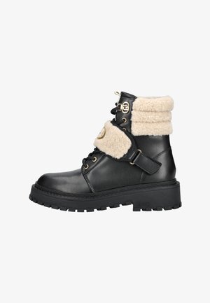 Stivaletto in pelle nera con suola dorsettata spessa, collo in shearling beige e cinturino, occhielli dorati e fibbia decorativa sul lato.