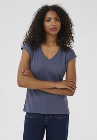 Mörkblå t-shirt med kort ärm och V-hals, gjord av mjukt tyg, med en avslappnad passform och en slät textur, ihop med mörka jeans.