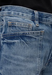 Πίσω όψη μπλε τζιν με ορατό θηλάκι ζώνης, μέση και μια μικρή πίσω τσέπη μέσα σε μια μεγαλύτερη πίσω τσέπη.