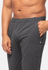 Grijze katoenen sweatpants met een elastische tailleband, zijzakken en een klein logo aan de linkerkant nabij de zak. Zachte textuur.