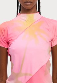 Cămașă cu mânecă scurtă în degrade roz și galben, cu un model floral. Prezintă un guler înalt și un design încrucișat în față, cu o textură fină.