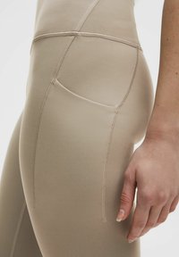 Leggings beige con una texture liscia e elastica, dotati di una tasca laterale, cuciture piatte e un design aderente che si adatta alla silhouette del corpo.
