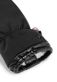 Schwarzer Handschuh mit weichem Stoff, Lederakzenten, elastischem Bündchen und einem kleinen Markenschild. Das Innere ist mit weichem Material gefüttert für zusätzlichen Komfort.