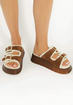 Sandales à plateforme brunes avec doublure en fourrure, dotées de doubles boucles sur la sangle et d'un design à bout ouvert. Semelle texturée pour une meilleure adhérence.