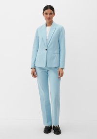Completo su misura azzurro chiaro con chiusura a un pulsante, revers a punta e pantaloni slim-fit. Tessuto liscio; indossato con scarpe nere.