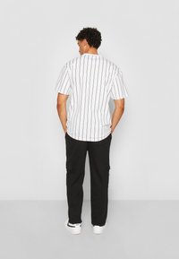 Short-sleeve shirt in white with black vertical stripes, paired with black cargo pants and white sneakers, showing a simple, casual design.