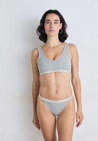 Pilkos medvilnės sportinė liemenėlė ir atitinkamos kelnaitės, turinčios plačią elastingą juostą su "Calvin Klein" logotipu. Paprastas dizainas, minimalus aparatūra.
