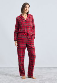 Rød ternet pyjamassæt med lange ærmer, knaplukning og matchende bukser med elastikliv. Blødt stof med grønne og sorte detaljer.