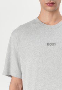 Tricou din bumbac gri cu gât rotund și mâneci scurte. Prezintă un logo „BOSS” în relief de culoare gri pe piept. Textură moale.